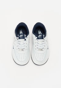 Baskets Nike Force 1 blanches avec des accents bleu marine, boîte à orteils perforée, lacets plats et col rembourré. Semelle en caoutchouc avec un motif texturé.