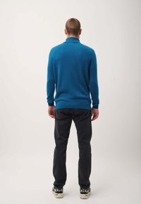 Maglione turchese con colletto alto, realizzato in materiale morbido, abbinato a jeans neri e sneakers, visto da dietro.