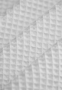 Weiße Stoff mit Waffelmuster und strukturierter Oberfläche, der eine Reihe erhabener Quadrate vor einem glatten Hintergrund präsentiert.