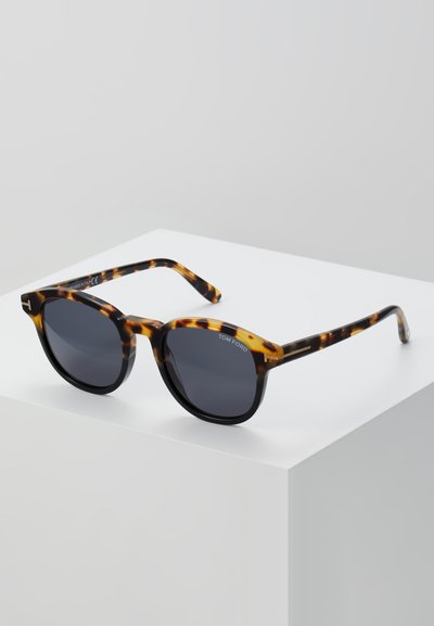 Tortoiseshell zonnebril met ronde monturen, donkere lenzen en slanke armen. Bevat het Tom Ford-merk op de lens en de arm.