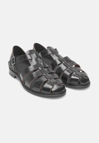 Sandali in pelle nera con fasce incrociate e design open toe, dotati di cuciture a contrasto marroni e una fibbia laterale per la regolazione.