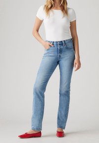Jeans de mezclilla azul claro con cintura ajustada, piernas rectas y un ligero desgaste. Combinados con una camiseta blanca ajustada y bailarinas rojas.