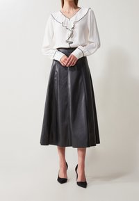 Vit blus med svarta volangdetaljer, kombinerad med en svart midikjol i läder. Svarta högklackade skor fullbordar outfiten.