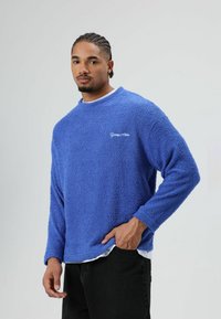 Blauwe fleece-trui met een zacht, gestructureerd oppervlak, voorzien van lange mouwen en een ronde hals. Geborduurd logo op de borst.