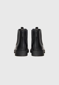Botas de cuero negras hasta el tobillo con dos cremalleras traseras, suelas gruesas y una textura suave. El diseño presenta acentos minimalistas.