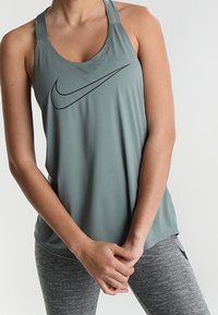 Lichtgroene sporttanktop met een ronde hals, dunne bandjes en een zwarte Nike-logo. Gladde stof, een ontspannen pasvorm en een licht gebogen zoom.