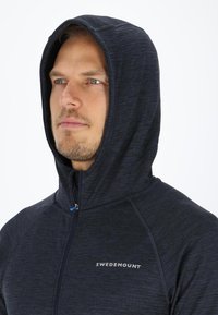 Dark blue hooded sweatshirt with a zip front and logo. Features a textured fabric, raglan sleeves, and a fitted design.