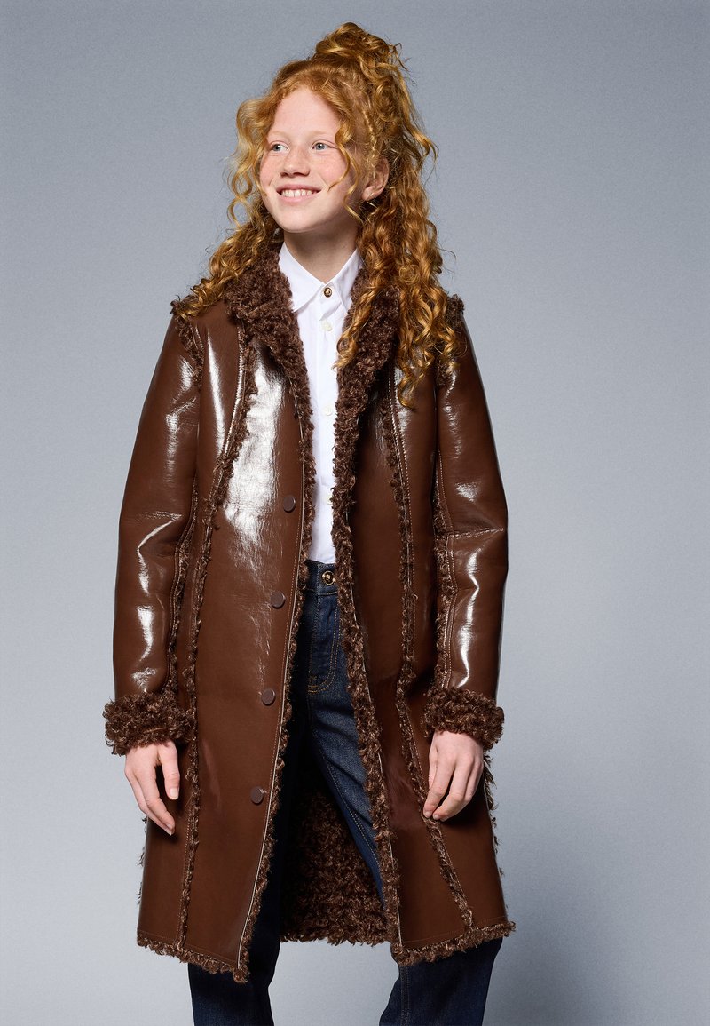 Brown faux leather coat with fur trim and lining, button closure, and textured, shaggy accents along the edges.