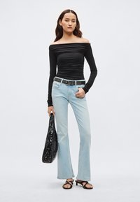 Zwarte off-shoulder top met lange mouwen, lichtblauwe wijde jeans, zwarte gespette riem, zwarte plastic tas, zwarte sandalen. Overal gladde texturen.