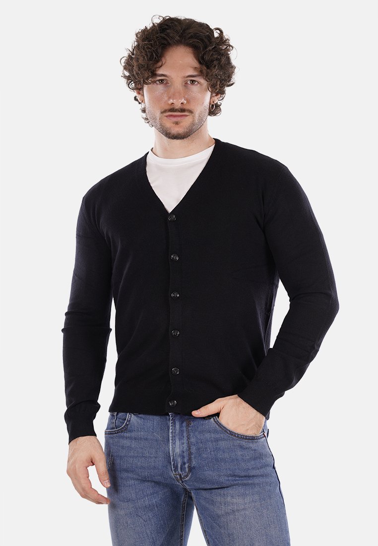 Cárdigan negro hecho de una tela suave, con cuello en V, mangas largas y seis botones en la parte delantera. Llevado sobre una camisa blanca, con un diseño ajustado.