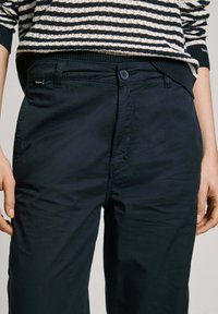 Pantalones azul marino de tejido ligero con una textura suave, cierre de botón y bolsillos laterales. Presentados con una blusa de punto a rayas.
