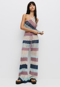 Gehaakt twee-delig outfit met een asymmetrische top en brede broekspijpen. Gestreept patroon in pastelkleuren: blauw, roze en crème.