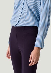 Hellblau und weiß gestreiftes Hemd mit Knopfleiste und Manschetten, kombiniert mit dunkelblauen maßgeschneiderten Hosen mit vorderen Nähten.