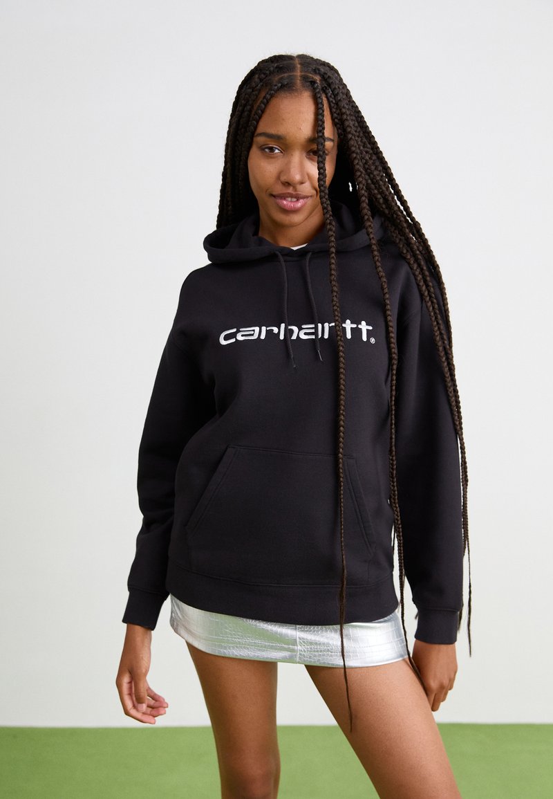 Felpa nera con logo bianco "carhartt", tasca a marsupio, lacci e polsini a costine; abbinata a una mini gonna argentata lucida.