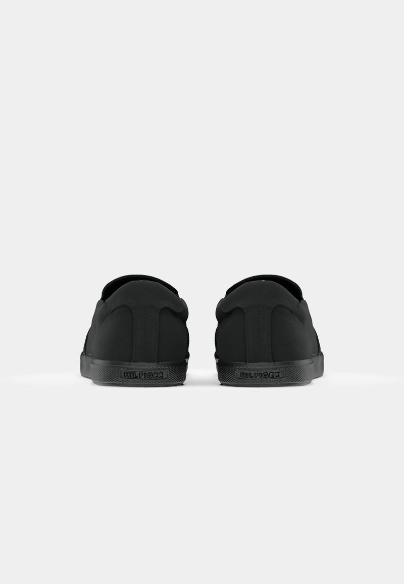 Baskets noires avec une tige en textile lisse, un dos arrondi, des détails de couture subtils et une semelle en caoutchouc texturée. Marque visible sur le talon.