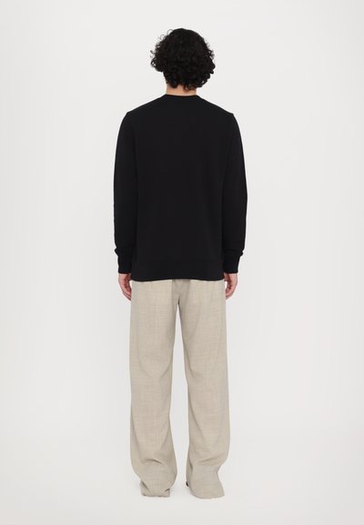 Sort sweatshirt med rund hals og ribbede manchetter, parret med lysebeige, løstsiddende bukser. Glat stof, minimalistisk design.