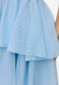 Gaiši zila slāņota kleita ar krokotu, caurspīdīgu auduma tekstūru, ar plandošu svārku un maigu, plūstošu dizainu. Akcentēta ar smalkiem šuvumiem.