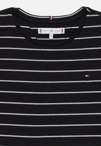 Čierne rebrované tričko s bielymi horizontálnymi pruhmi. Má okrúhly výstrih a malé vyšívané logo na hrudi. Obsahuje štítok.