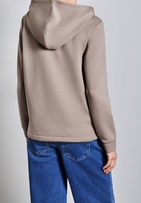 Felpa con cappuccio in morbido tessuto beige, con polsini a coste, orlo arrotondato e una vestibilità rilassata. Abbinata a jeans azzurri a gamba larga.