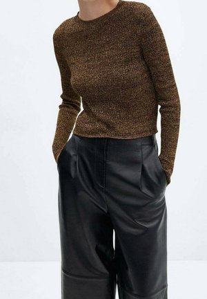 Persoon draagt een bruin gebreid longsleeve top, ingestopt in high-waisted, losse zwarte leren broek met handen in de zakken.