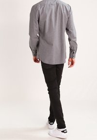 Lys grå skjorte med knaplukning og et tekstureret mønster, parret med sorte slim-fit jeans og hvide sneakers med et sort logo på hælen.