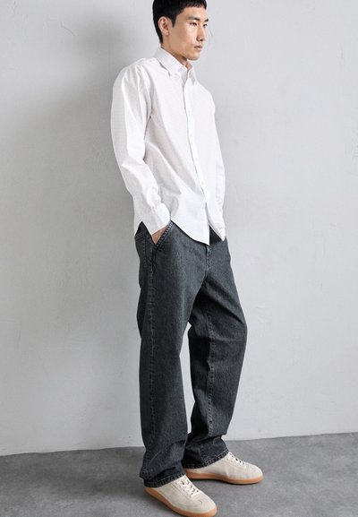 Vit långärmad skjorta med en subtilt mönster, ihopparad med löst sittande mörkgrå jeans och beige sneakers med ljusbruna sulor.