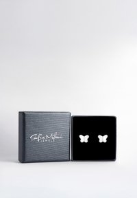 Orecchini d'argento a forma di farfalla su un'esposizione in velluto nero all'interno di una scatola nera opaca con un logo sul coperchio. Design semplice ed elegante.