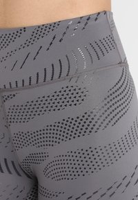 Leggings grigi alti in vita con un mix di motivi a pois e triangoli, caratterizzati da una texture liscia e una leggera lucentezza in diverse sfumature di nero.