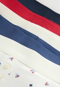 Stos złożonych prążkowanych taśm materiałowych w kolorach granatowym, czerwonym, białym i niebieskim na kremowym materiale z małym kwiatowym wzorem i guzikami.