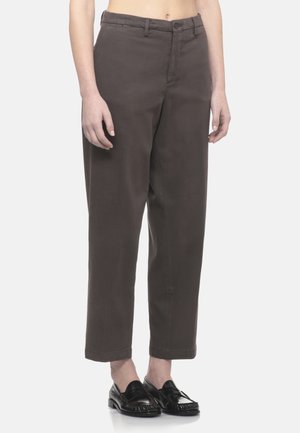 Persona che indossa pantaloni marrone scuro a gamba dritta e vita alta con chiusura a bottone, abbinati a mocassini neri slip-on.