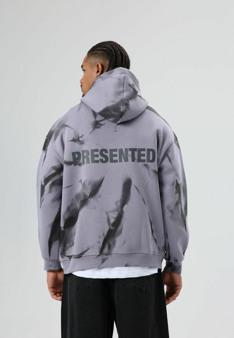 Oversized grijze hoodie met zwart tie-dye patroon, met het woord "PRESENTED" in dikke zwarte letters op de achterkant. Zacht materiaal, capuchonontwerp.