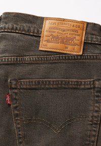 Los jeans de mezclilla de Levi's presentan una etiqueta de cuero marrón con la marca en relieve, costuras naranjas y una etiqueta roja en el bolsillo, en un lavado oscuro.