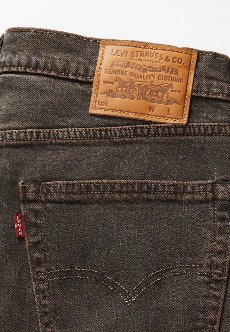 Levi's Denim-Jeans haben ein braunes Leder-Patch mit eingeprägtem Branding, orangefarbene Nähte und ein rotes Tab an der Tasche, in einem dunklen Waschton.