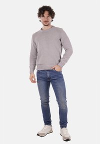 Maglione a maglia grigio chiaro, colletto a giro, polsini e orlo a coste, abbinato a jeans blu e sneakers bianche con dettagli grigi.