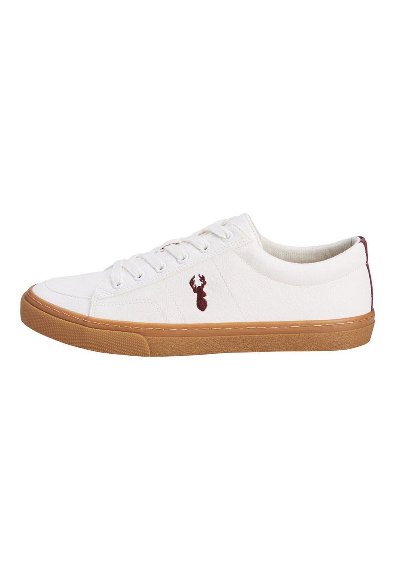 Zapatilla blanca de caña baja con suela de goma, cordones blancos y pequeño logo de ciervo en color marrón en el lado, mostrada desde la vista lateral exterior.