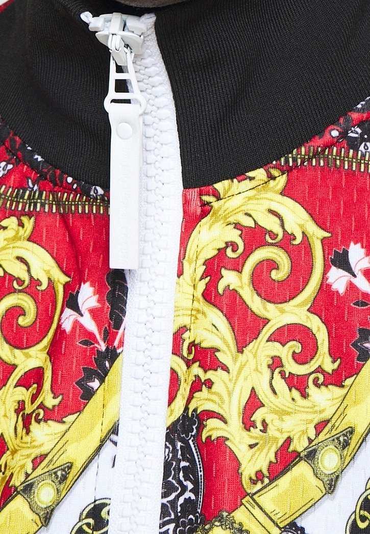 Gros plan sur une fermeture éclair blanche sur un tissu noir et rouge orné de motifs baroques jaunes et noirs complexes.