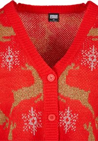 Röd stickad cardigan med V-hals, guldrenmönster och vita snöflingor. Den har en texturerad finish och röd knappstängning.