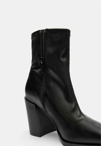 Stivale alla caviglia nero realizzato in pelle liscia, dotato di una cerniera laterale, punta quadrata e tacco spesso. Design elegante con dettagli di cucitura minimi.