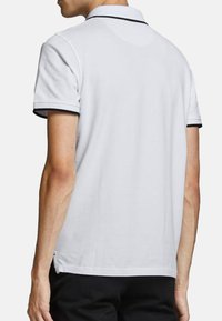 Witte poloshirt met een standaard kraag, zwarte trim op de mouwen en kraag, korte mouwen en een rechte zoom. Gemaakt van lichtgewicht stof.