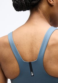 Κοντινό πλάνο του άνω μέρους της πλάτης ενός ατόμου που φοράει μπλε αθλητικό τοπ με το λογότυπο The North Face στο κεντρικό λουράκι της πλάτης.