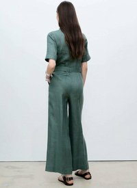 Grön, lätt jumpsuit med korta ärmar, vida ben och resårmidja. Strukturerad tyg och minimalistisk design, sedd bakifrån.