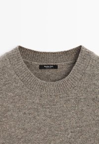 Maglione grigio a collo rotondo lavorato a maglia con colletto a coste e un'etichetta nera con scritto "Massimo Dutti Made in China."