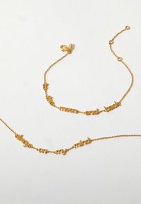 Guldtonet vedhængs halskæde med mellemrum mellem bogstaverne, der danner sætningerne "til månen og tilbage" og "altid på mine tanker," med en delikat kæde.