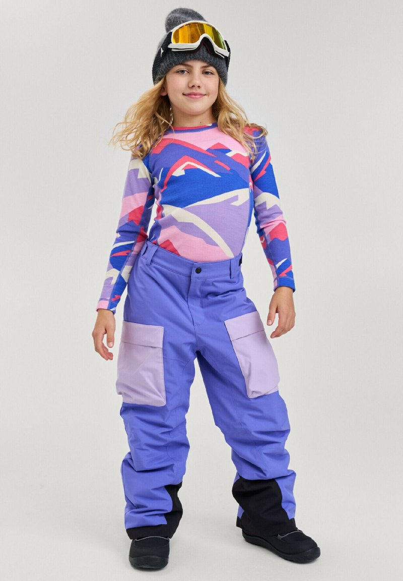 Ski outfit featuring a multicolored patterned long-sleeve shirt and purple ski pants with light purple pockets; worn with a black beanie and goggles.