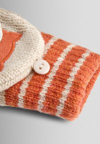 Suurendatud vaade oranži ja koorevärvi kudumiskangale, millel on valged zikk-zakk triibud, ning koorevärvi nööp õmmeldud manseti äärele.