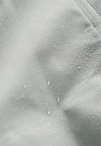 Gouttelettes d'eau perlant sur un tissu imperméable gris clair, mettant en valeur la texture hydrofuge du tissu et les détails des coutures.