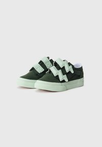 Baskets pour enfants vertes foncées avec un zigzag vert clair et des fermetures à double sangle sur fond blanc.