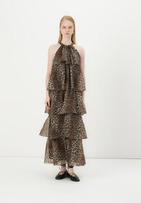Leopardų rašto maksi suknelė su sluoksniuotais raukiniais, kaklo ryšimo dizainu ir permatomu audiniu. Juodi bateliai iki kulkšnies užbaigia įvaizdį.