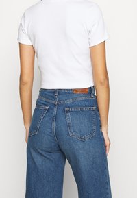 White cropped t-shirt paired with high-waisted blue denim jeans, featuring a classic five-pocket design and a brown leather tag at the waistband.
