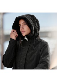 Černá voděodolná bunda s kapucí, která má hladký povrch a je poseta drobnými kapkami vody. Navržena pro venkovní nošení.